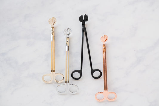 Deliciously Wickt metal candle wick trimmers in assorted finishes displayed on a light background.