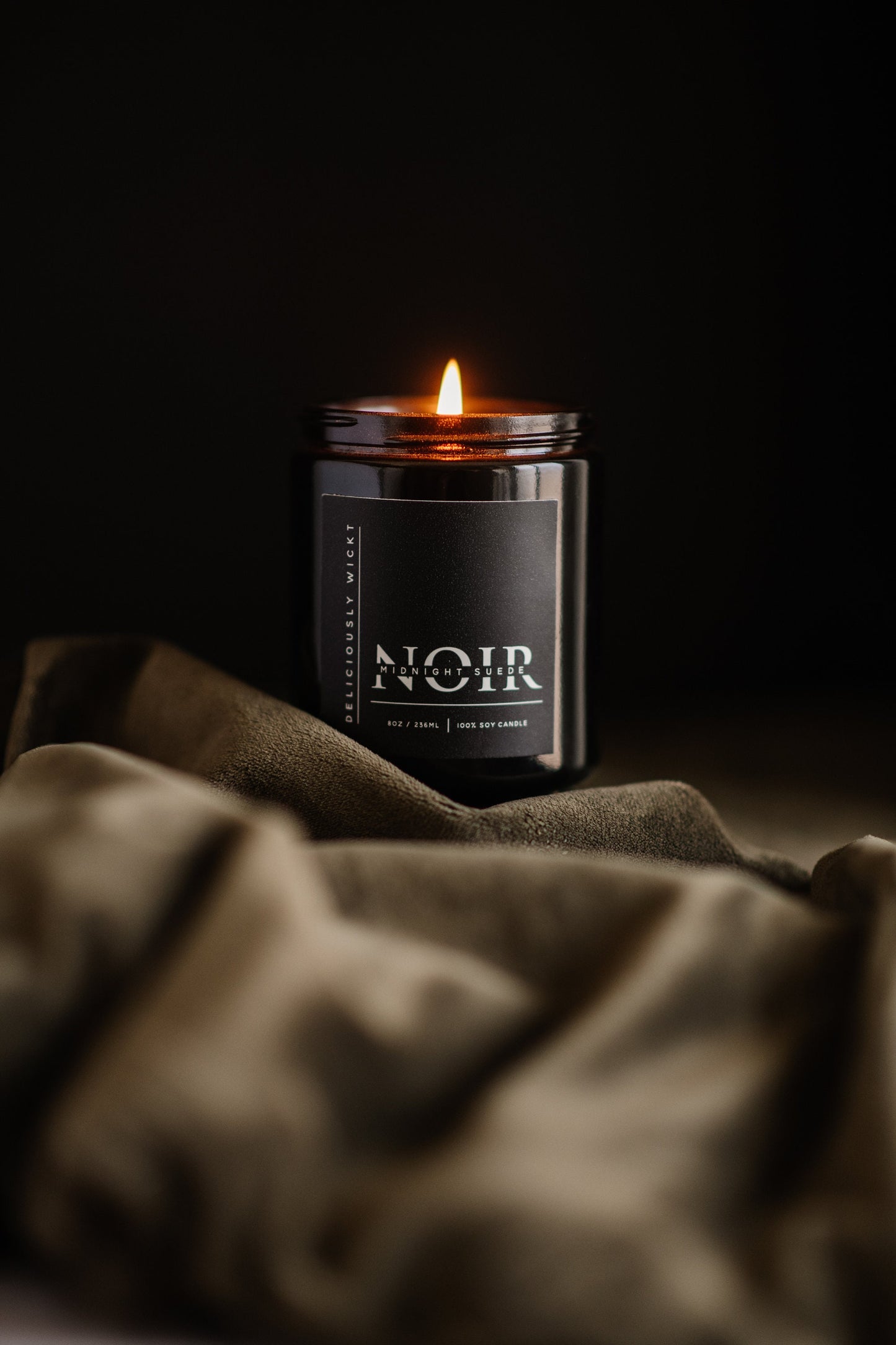 Midnight Suede black soy candle burning against a dark background