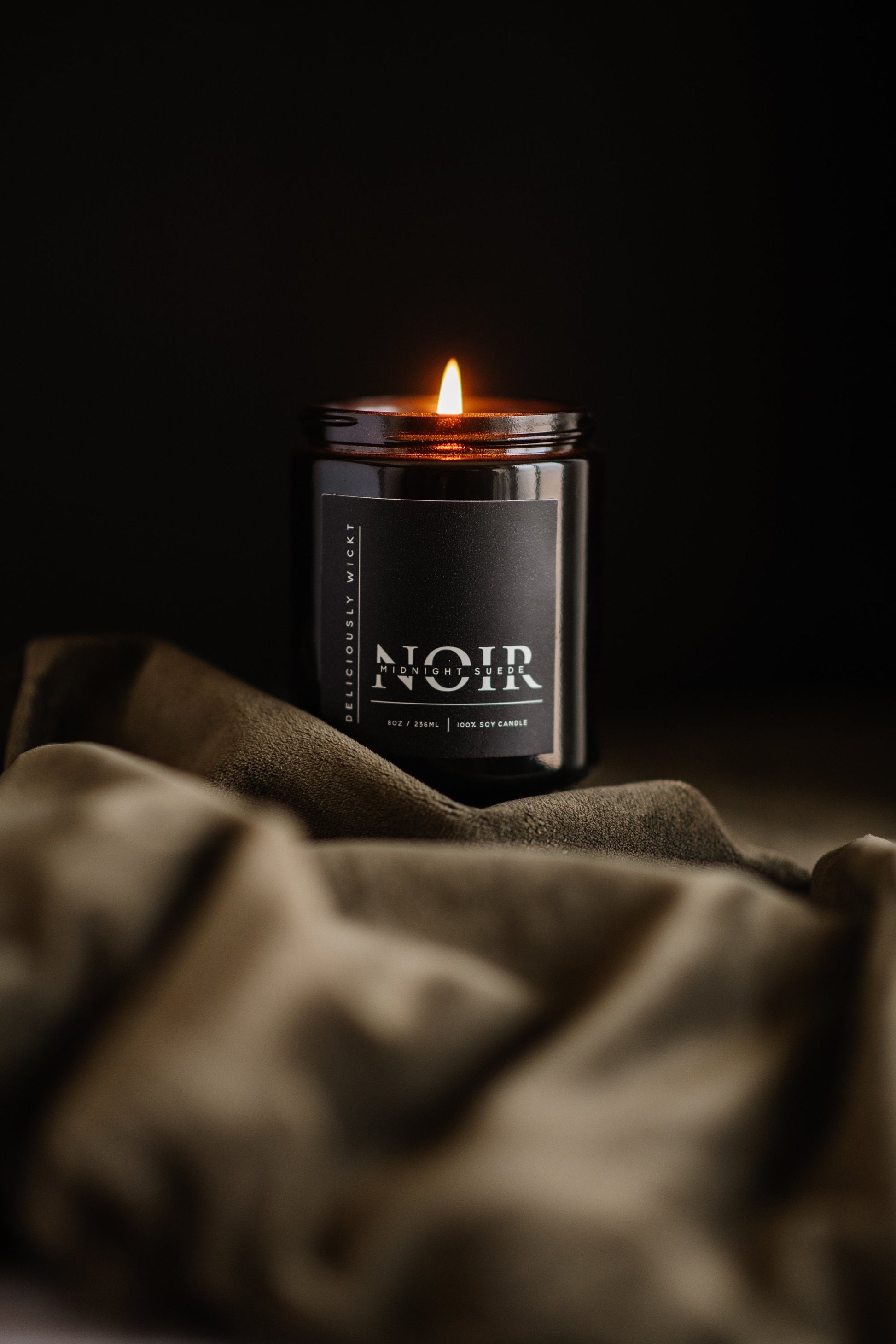 Midnight Suede black soy candle burning against a dark background