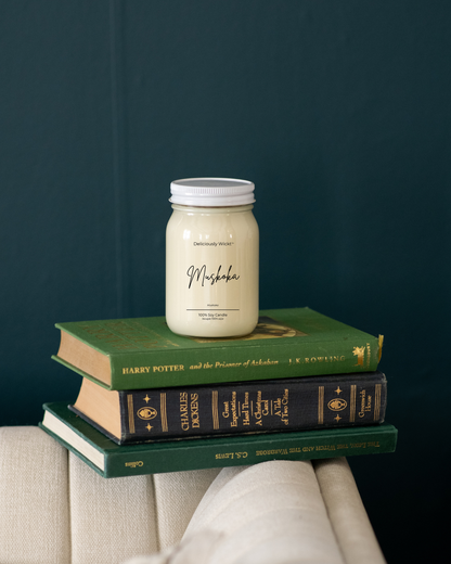 Deliciously Wickt Muskoka 16 oz mason jar soy candle displayed on stacked books against a dark teal wall.