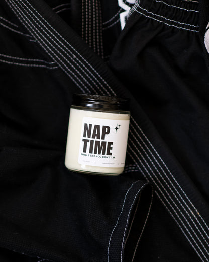 Nap Time Jiu-Jitsu soy candle with “Smells like you didn’t tap” label displayed on a black gi