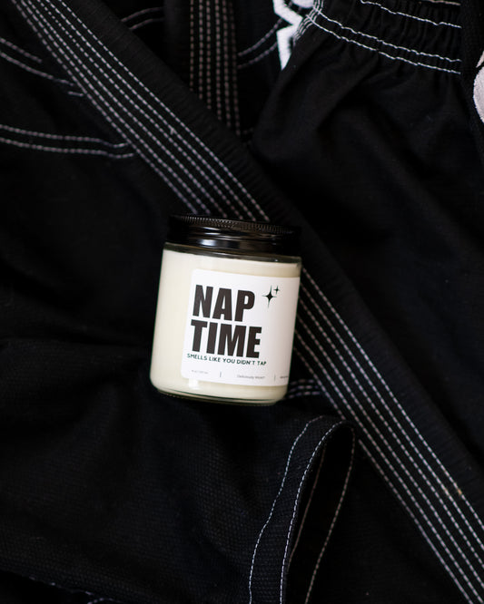 Nap Time Jiu-Jitsu soy candle with “Smells like you didn’t tap” label displayed on a black gi