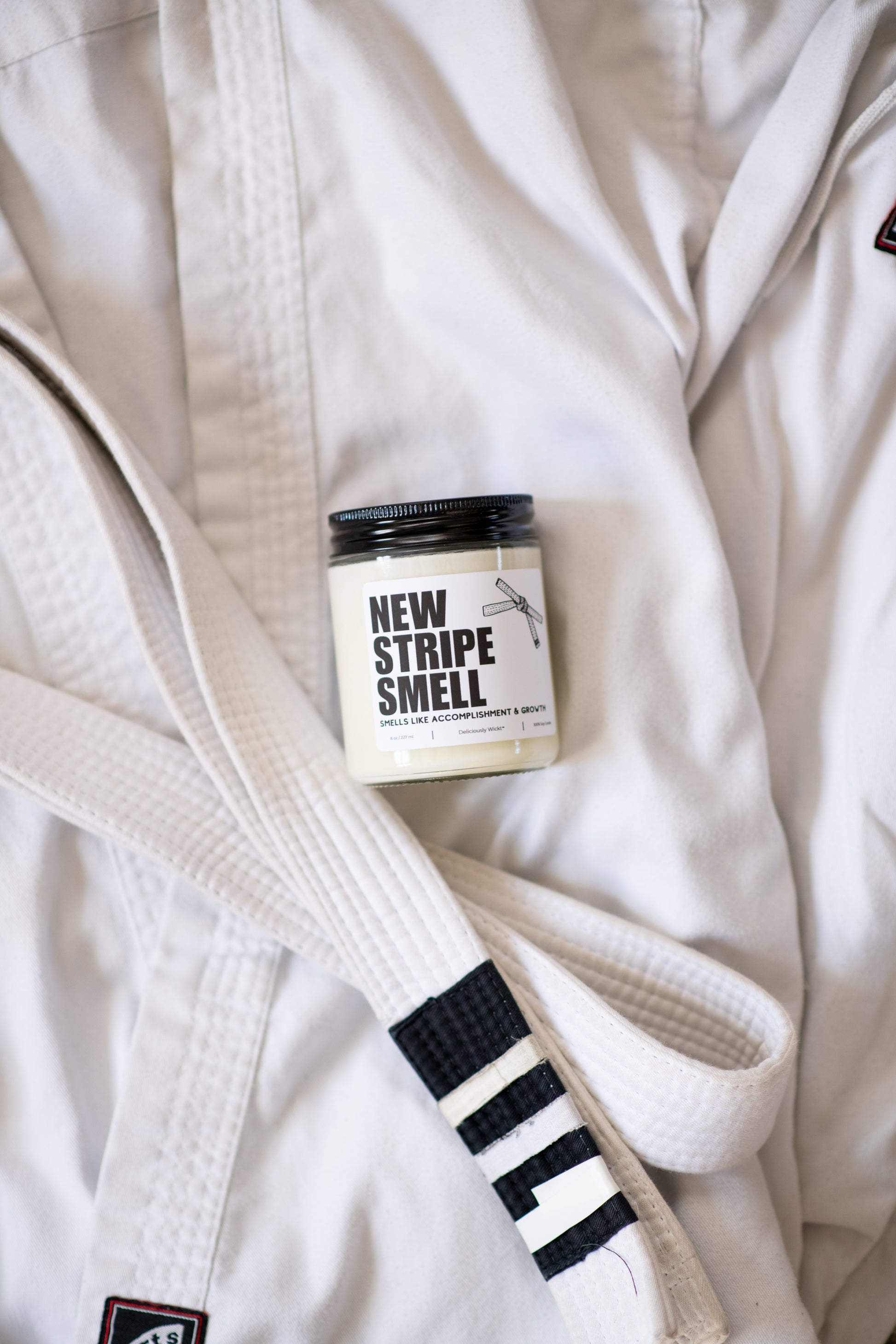 New Stripe Smell Jiu-Jitsu soy candle with “Smells like accomplishment & growth” label displayed on a gi