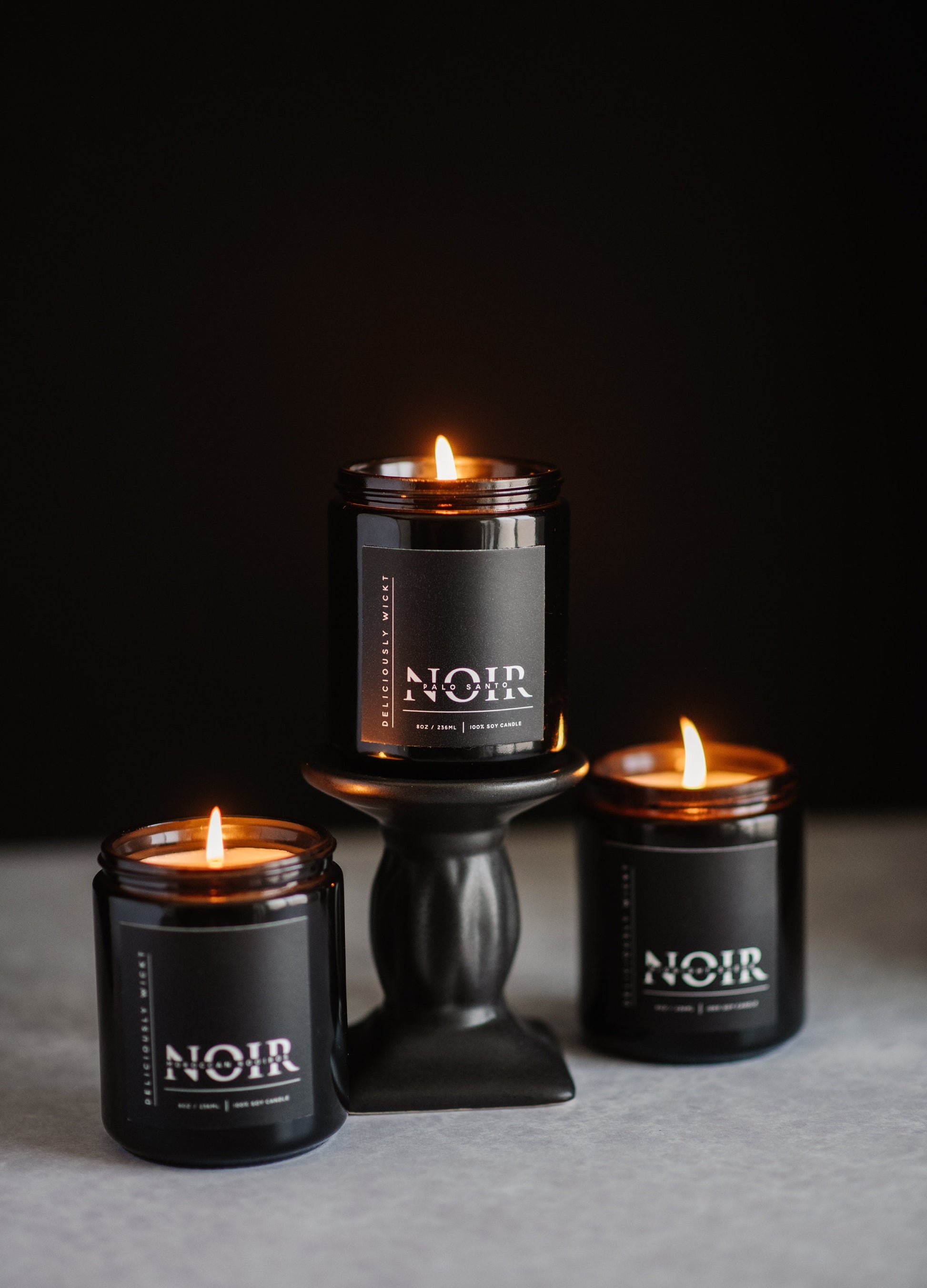 Three NOIR soy candles burning together in matte black vessels