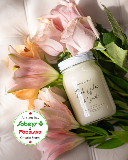 Deliciously Wickt Pink Lychee & Suede 16 oz mason jar soy candle displayed among pink flowers; Sobeys and Foodland Ontario badge.