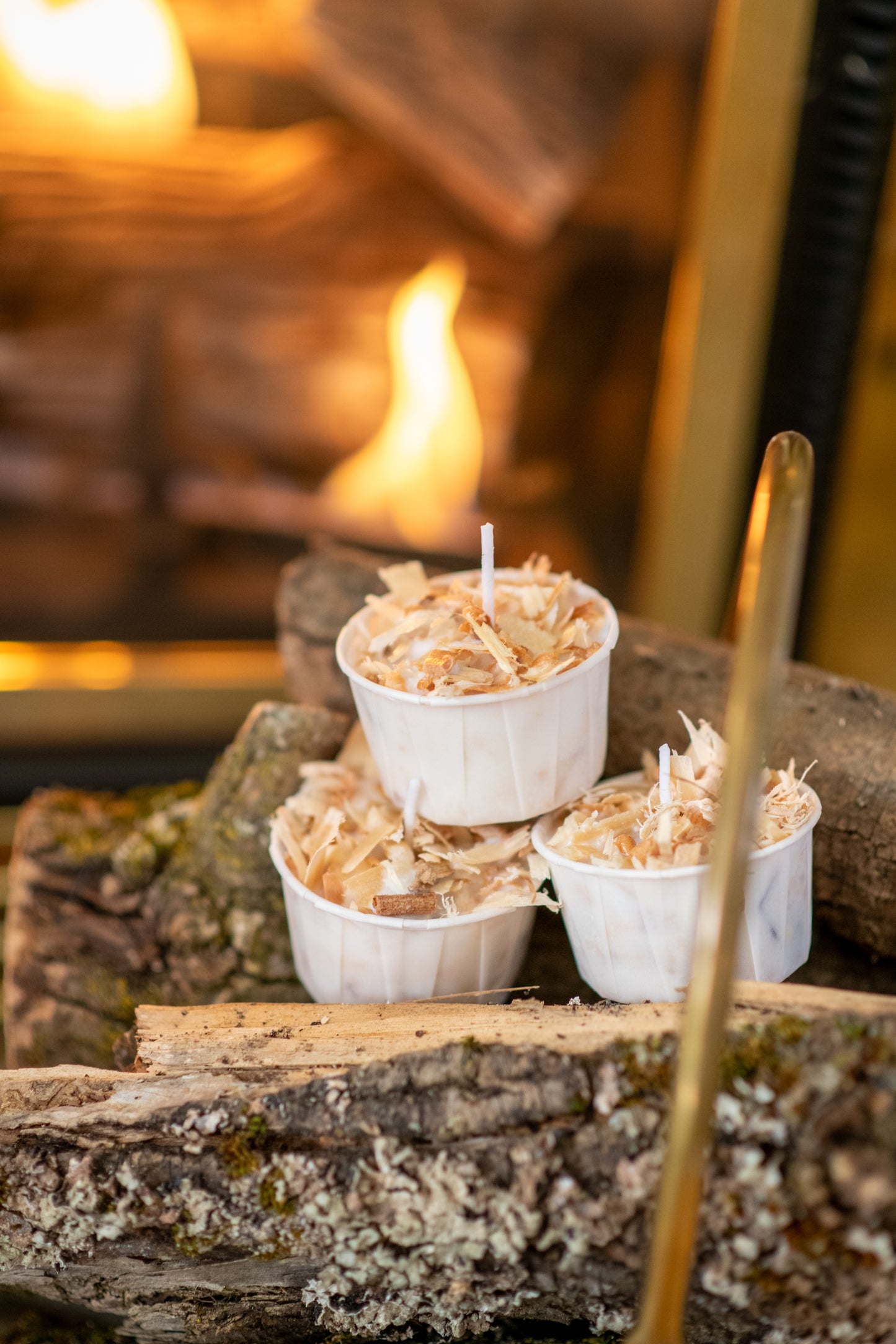 Deliciously Wickt Torcht firestarter pods displayed on stacked firewood beside a burning fireplace.