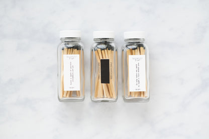 Deliciously Wickt set of three clear glass bottles filled with long stick safety matches on a light marble surface.