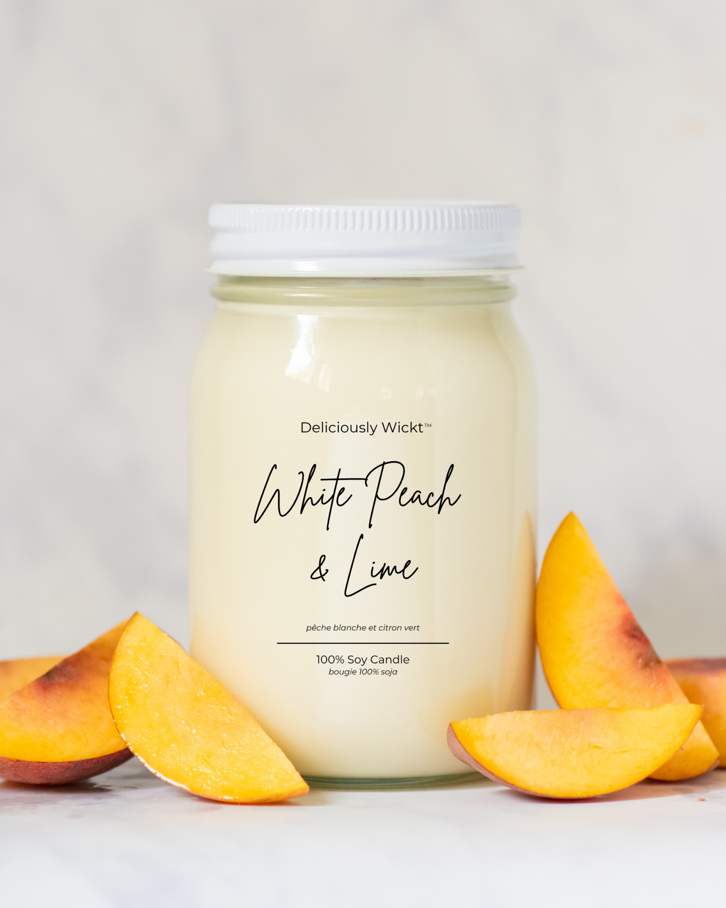 Deliciously Wickt White Peach & Lime 16 oz mason jar soy candle displayed with fresh peach slices on a light background.