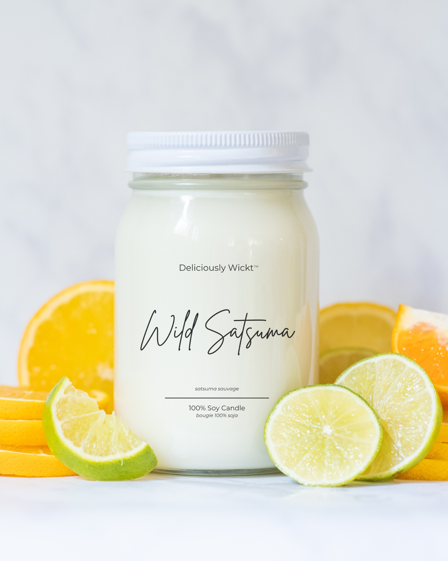 Deliciously Wickt Wild Satsuma 16 oz mason jar soy candle styled with fresh orange slices and lime wedges on light marble.