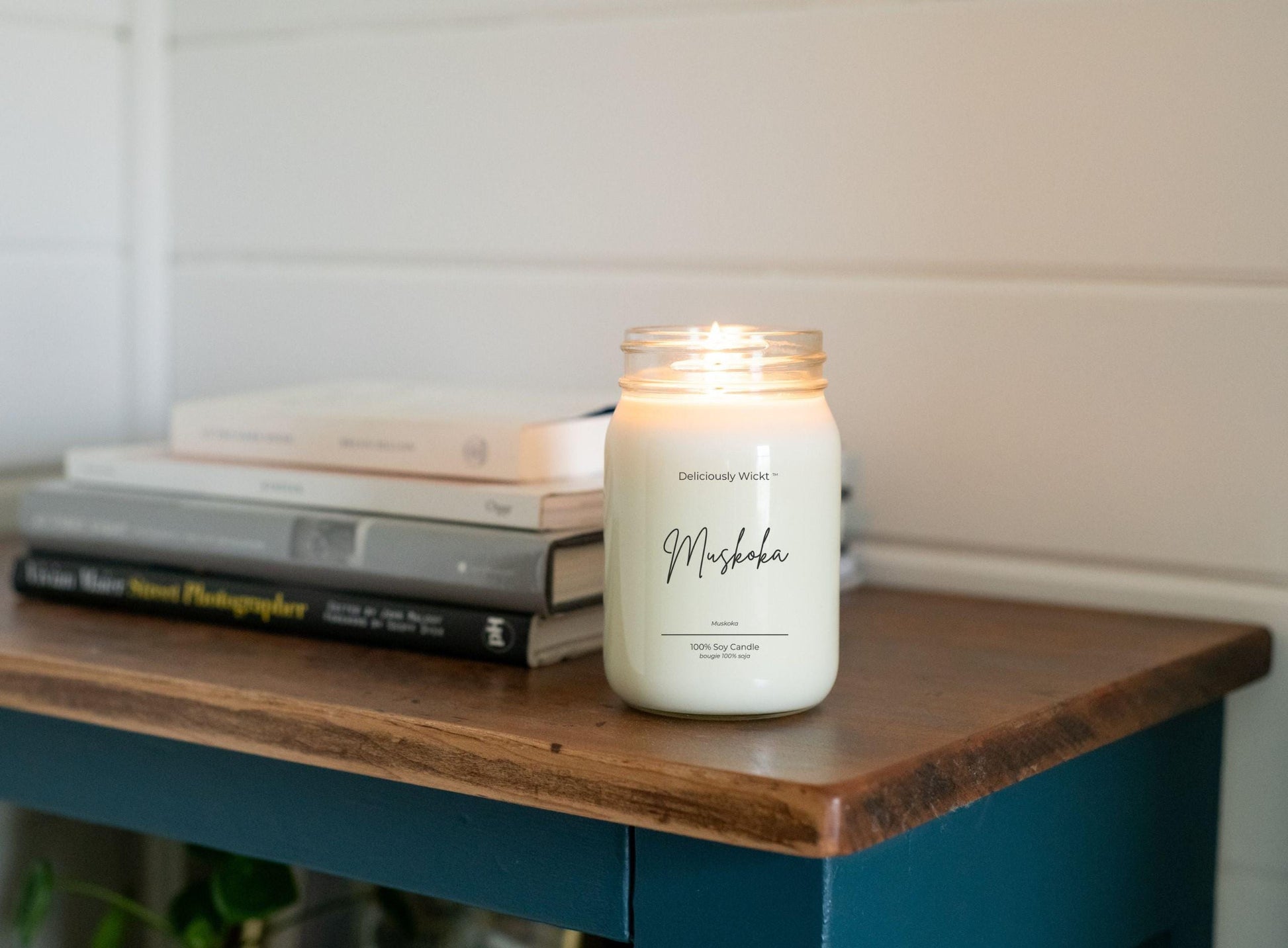 Candle labeled 'Muskoka' on a wooden surface with books in the background